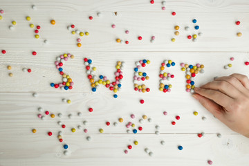 Closeup image of woman making word Sweet from colorful candies