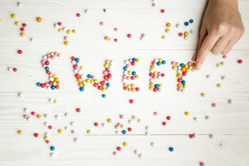 Closeup image of woman making word Sweet from colorful candies