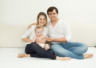 Happy young family posing with baby son on bed