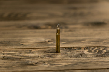 Closeup image of Kalashikov riffle bullet on old wooden desk