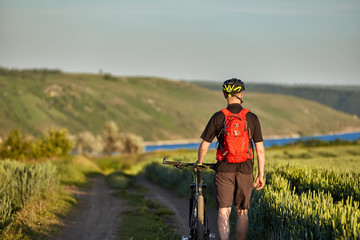 Rear view of the young cyclist riding bicycle on the road of the field.