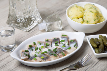 Pieces of herring with onions, gherkins, boiled potatoes and vodka. Selective focus