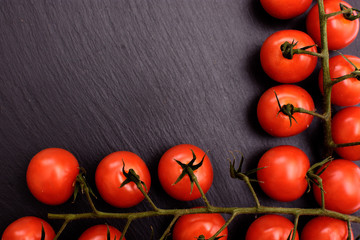 Red cherry tomatoes lie on a black stone slate board, background