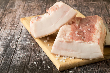 
Pork lard.   Two pieces of raw pork lard on a wooden cutting board.