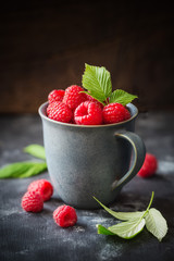 Cup full of fresh ripe garden raspberries against dark rustic background. Shallow DOF