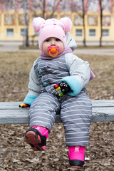 Baby with a pacifier sitting on a bench
