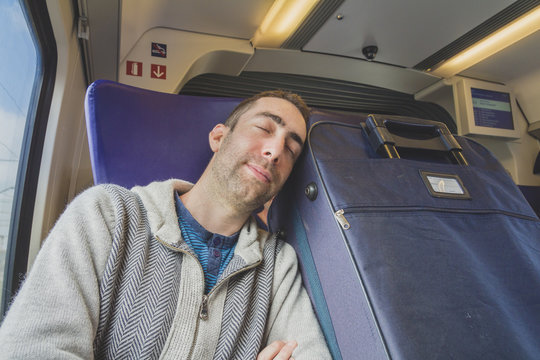 Young man traveling on a train and sleep on blue suitcase next to him