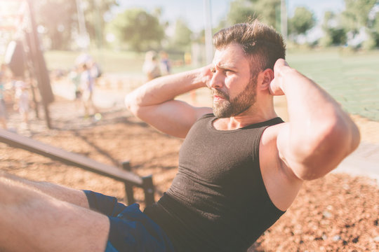 Muscular man exercising doing sit up exercise. Athlete with six pack, white male, Outdoor training. Sports and healthy lifestyle. Bearded black-haired guy doing crunches Outdoors
