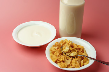 Corn flakes and yogurt in white bowl  with milk bottle place on pink background