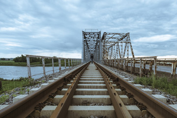 A man walks the old train bridge over a river.