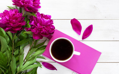 A cup of coffee with a notebook, pen and flowers peonies on a white table. Female objects for work view from above with copy space.