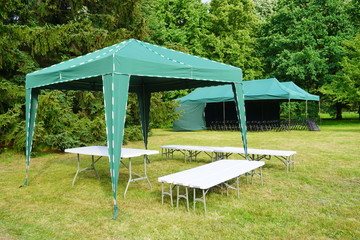 Green garden tent, garden pavilion. Rest area with  chair and picnic tables and green tent installed on green lawn in a park   © skorpionik00