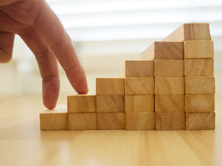 Woman fingers climbing on construction of wood block stacking as step stair on wood floor. Concept...