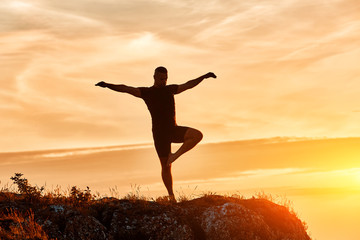 Silhouette of the man practicing yoga on the hill against beautiful sunset.