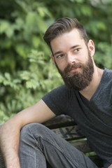 Thoughtful bearded guy sitting on a bench in park