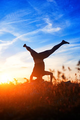 Young man practicing yoga and stretching on a rock at sunset light.