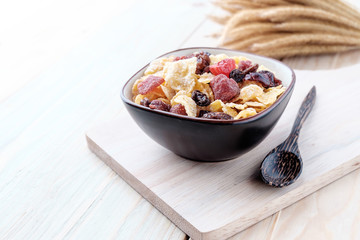 cornflakes and dry berry fruits in a brown bowl on a wooden background.
