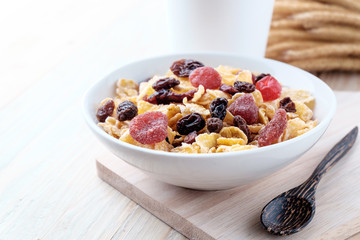 cornflakes and dry berry fruits in a white bowl on a wooden background.