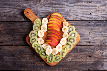 Cut kiwi, banana and nectarine lying on a cutting board.