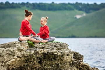 Mother and daughter in the lotus position on the rock above big river.