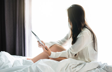 Asian woman use a tablet on the bed after wake up in weekend mornning.Use the tablet to read news, watch movies, or chat in relex and Communications, social media concept.