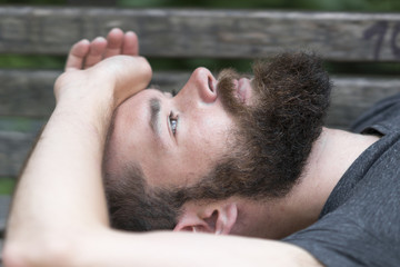 Fototapeta premium Handsome bearded guy resting laying on a bench in park