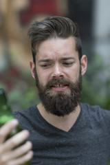 Handsome hipster holding a bottle of beer. Focus on his face on background
