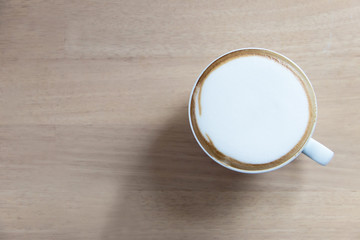 Hot cappuccino in white cup on wooden table with copy space