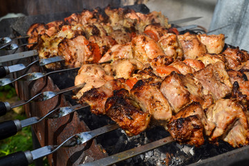 Grilled kebab cooking on metal skewer closeup. Roasted meat cooked at barbecue. Traditional eastern dish, shish kebab. Grill on charcoal and flame, picnic