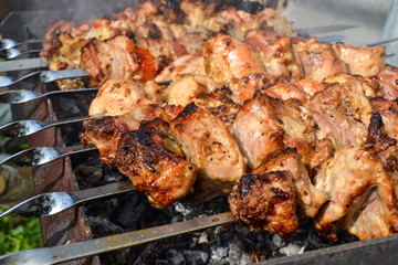 Grilled kebab cooking on metal skewer closeup. Roasted meat cooked at barbecue. Traditional eastern dish, shish kebab. Grill on charcoal and flame, picnic