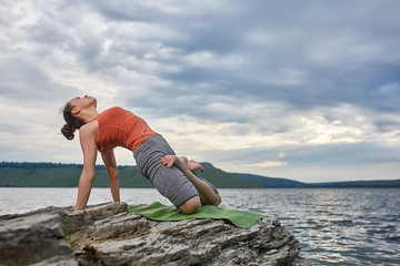 Young sporty woman doing different variants of yoga position on a rocky rivershore.