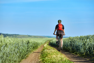 Rear view of the young cyclist with backpack cycling in the track of the field.