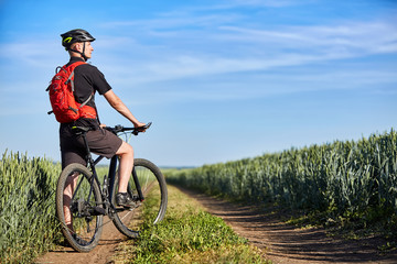Fototapeta na wymiar Attractive cyclist standing with mountain bicycle in field with blue sky on a background.