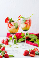 Alcoholic and non-alcoholic refreshing drinks, cold sparkling cocktail with ice, green mint and fresh strawberries in a beautiful glass on a light background 