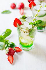 Alcoholic and non-alcoholic refreshing drinks, cold sparkling cocktail with ice, green mint and fresh strawberries in a beautiful glass on a light background 