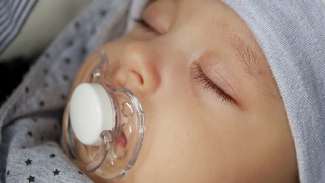 baby boy in hat four months with a pacifier sleeps in the stroller