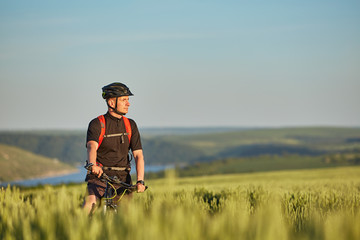 Attractive cyclist stands on the bike on the trail of the hay field in summer season.