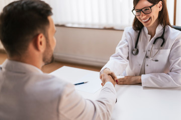 Smiling doctor at the clinic giving an handshake to his patient