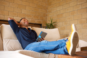 Relaxed young black man sitting in living room with digital tablet