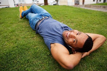 Close up happy young african man lying in grass and smiling