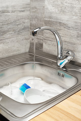 Kitchen sink with water, foam, tableware, blue cleaning sponge