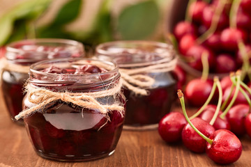 Cherry jam on wooden background in the jars