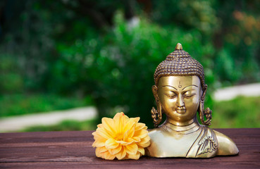 Golden antique Buddha statue on a blurred green background. Buddha and flowers. Concept religion. Copy space