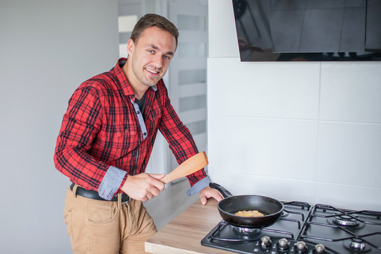 Young man in modern kitchen preparing dinner on frying pan.