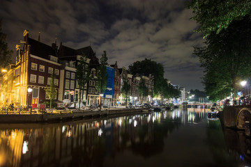Fototapeta na wymiar Beautiful traditional old buildings at night along the canal with reflection on water in Amsterdam, the Netherlands