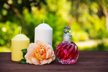 Obraz na płótnie Canvas Fragrant rose oil in a beautiful glass bottle. Pink elixir, candles and flowers. Spa concept. Romantic concept.