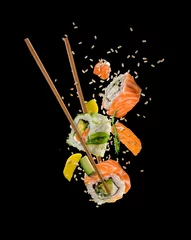 Vlies Fototapete Sushi-bar Sushi-Stücke zwischen Stäbchen auf schwarzem Hintergrund gelegt