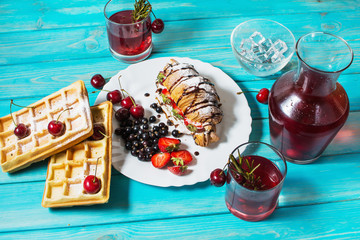 Breakfast : waffles and croissant with blueberries, cherries and strawberries. Stewed fruit in glasses and decanter.