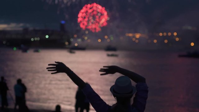 silhouette of a girl on the background of fireworks. the woman happily raises his hands and having fun on holiday