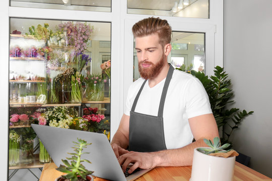 Young handsome florist working with laptop in flower shop